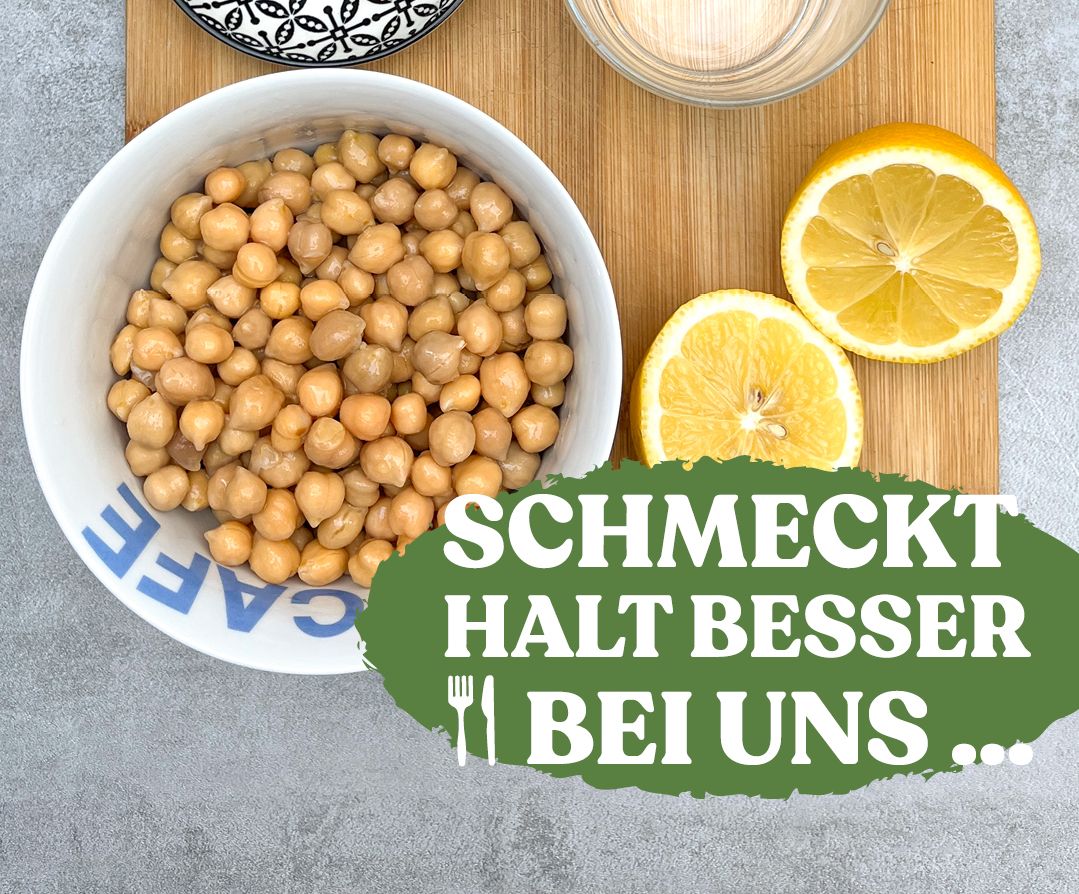 Zutaten für ein Hummus auf einem Holzbrett: Zitronen aufgeschnitten, Kichererbsen in einer Schale, Koblauch